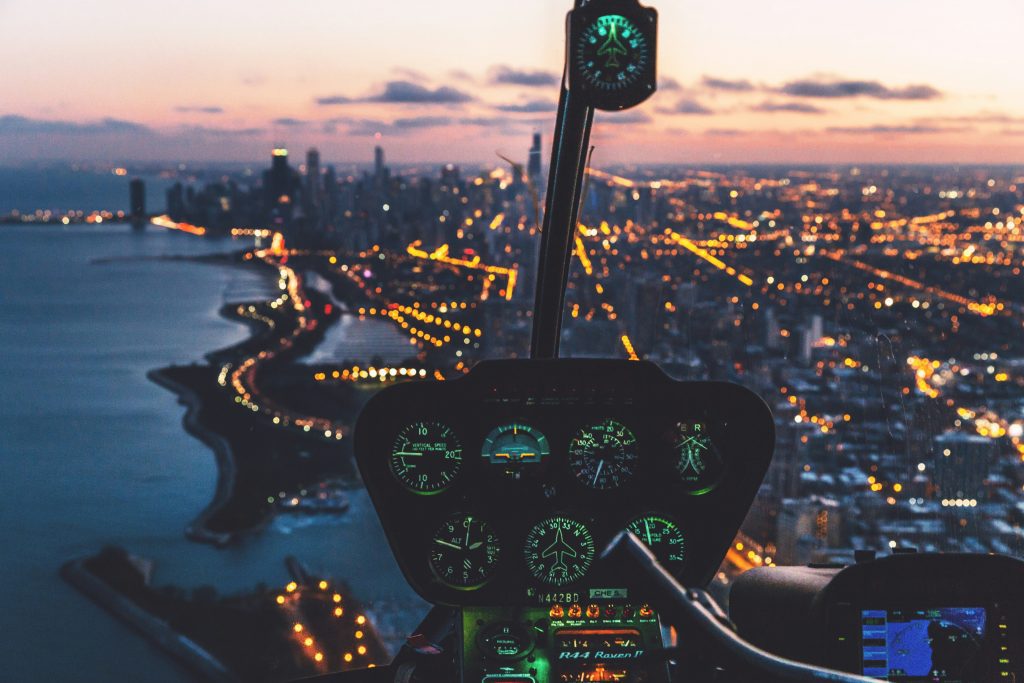 Helicopter cockpit view over the evening sky and night life.